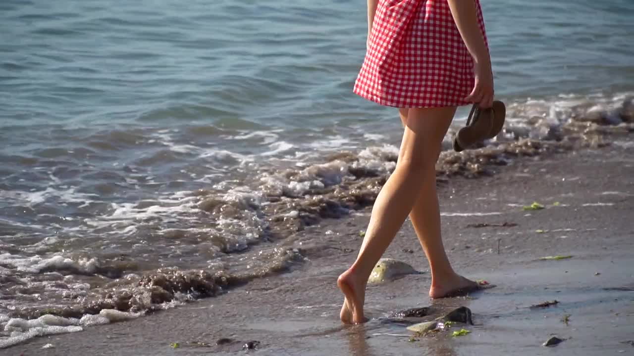 光着脚的女人在水里玩波浪。穿着旅游服装在海上度假的女人。在海边的水里，细腿和好天气。视频素材