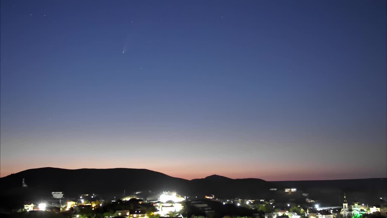 一颗彗星在黑暗的天空中，在星星之上的一个村庄在山脚下。视频素材