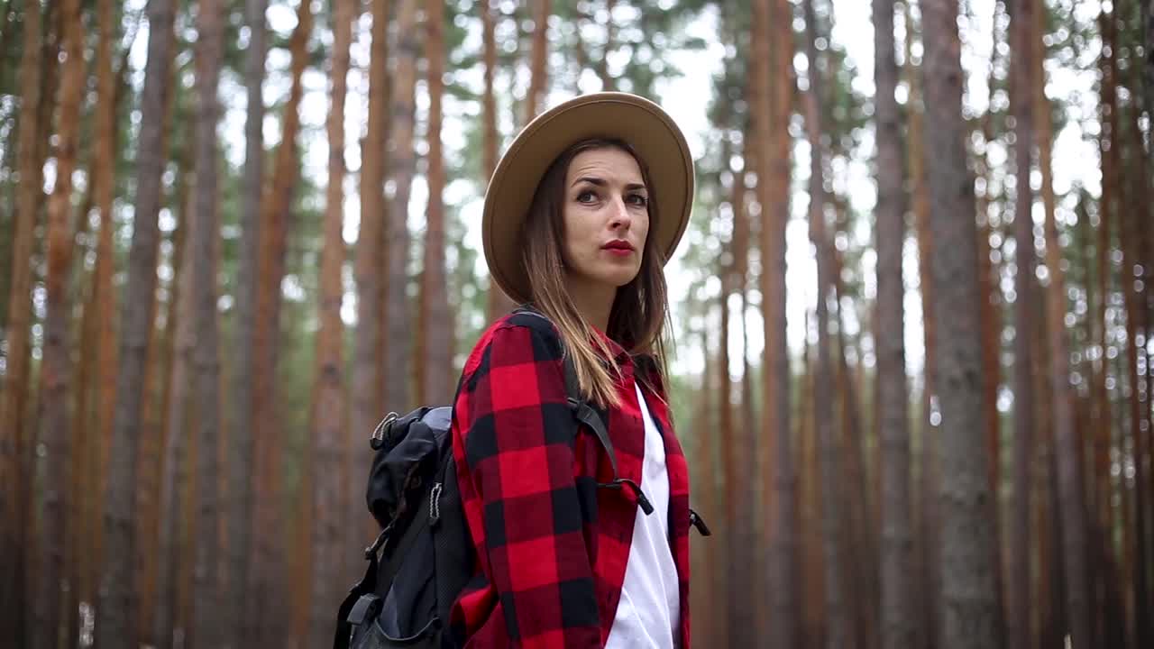 戴着帽子背着徒步背包的女人在森林里。概念的徒步旅行,旅游。视频素材