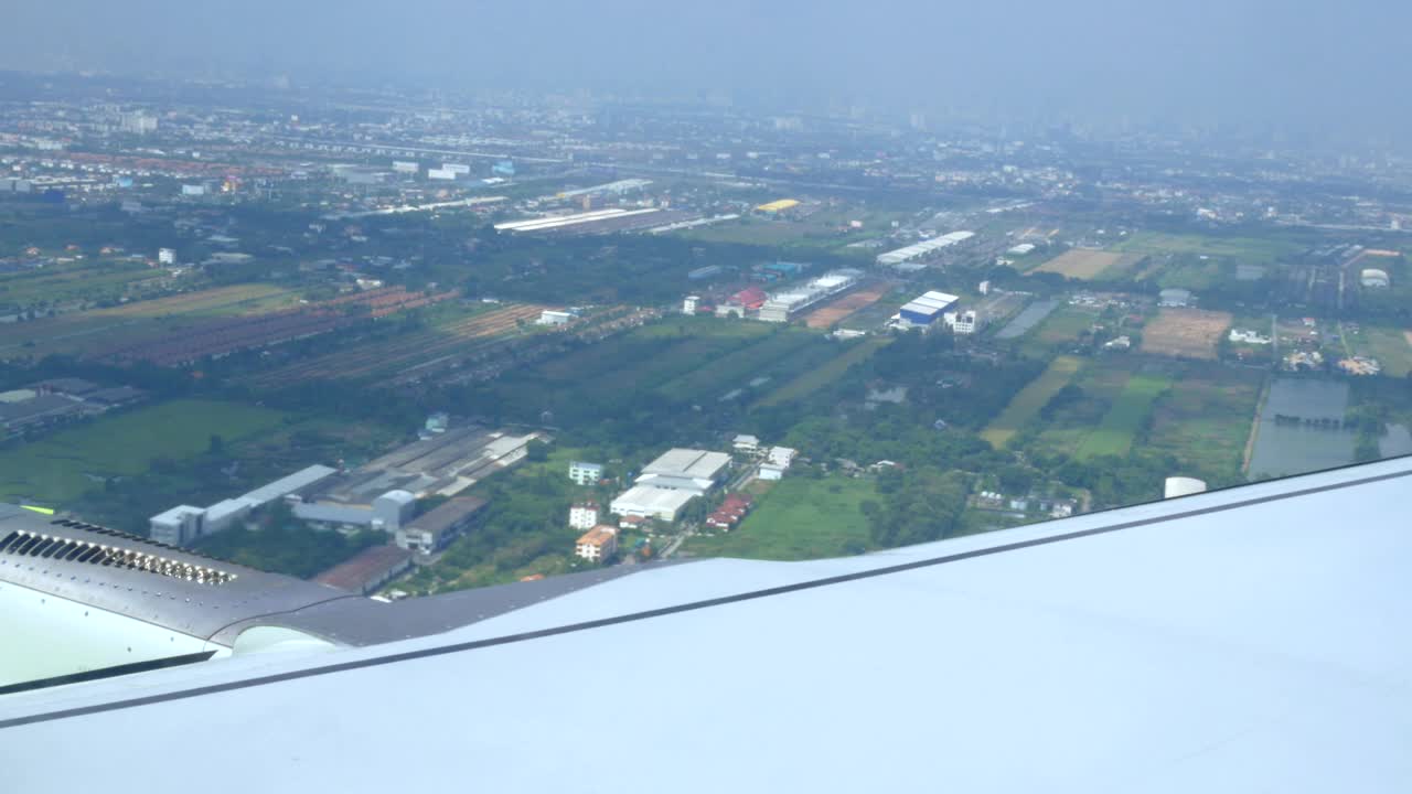 飞机从城市上空飞过。机翼下可见工业建筑和仓库。特写镜头视频素材