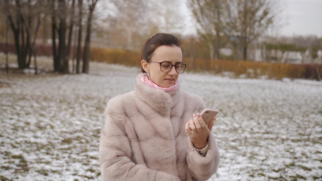 在下雪的冬天里，一个穿着皮大衣的漂亮女人在打电话视频素材