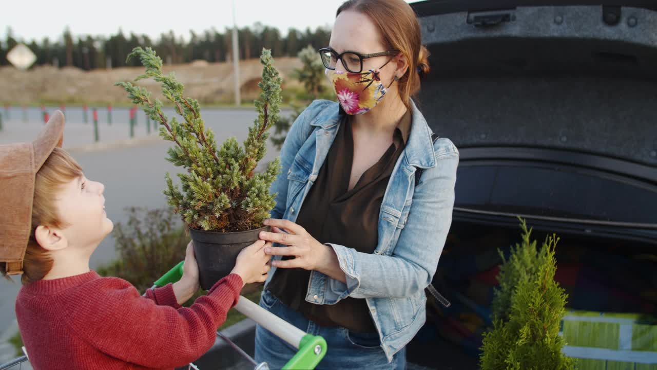 在花园中心购物后，家人在停车场把植物放进车里时戴上防护口罩视频素材