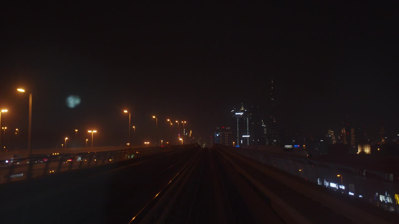 迪拜地铁在室外轨道上坡行驶。地铁在夜间行驶，背景是迪拜市中心的摩天大楼视频素材