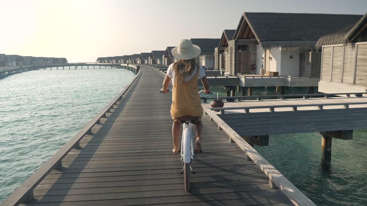 年轻女子骑着自行车在马尔代夫岛的旅游豪华度假村周围。视频素材