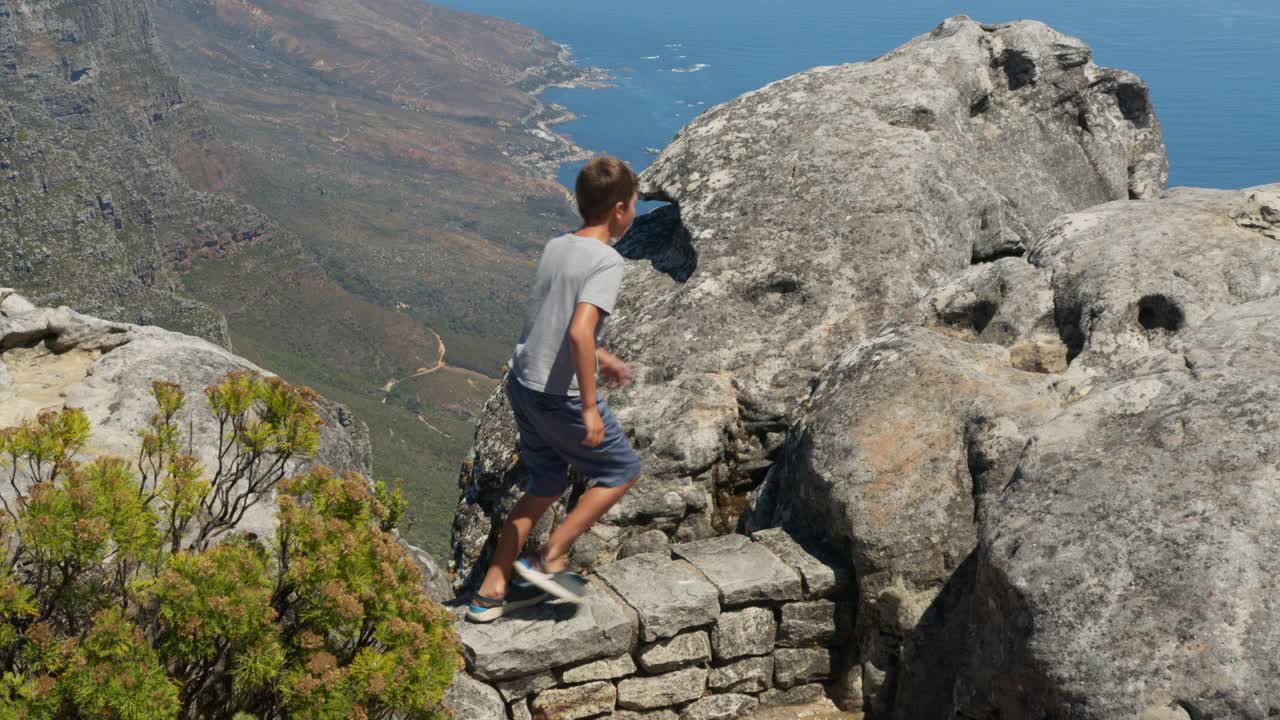 镜头跟随男孩在山顶上奔跑，在岩石上跳跃，在空中举起双臂，快乐而沉醉于生活，旅行和幸福。视频素材