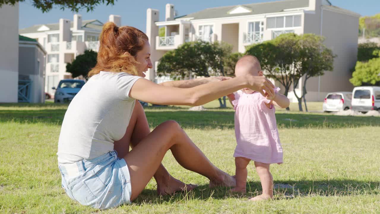 快乐的妈妈和宝宝在公园散步。漂亮的小女孩在妈妈的支持下站了起来。孩子跟着妈妈学走路。人生的第一步。视频素材