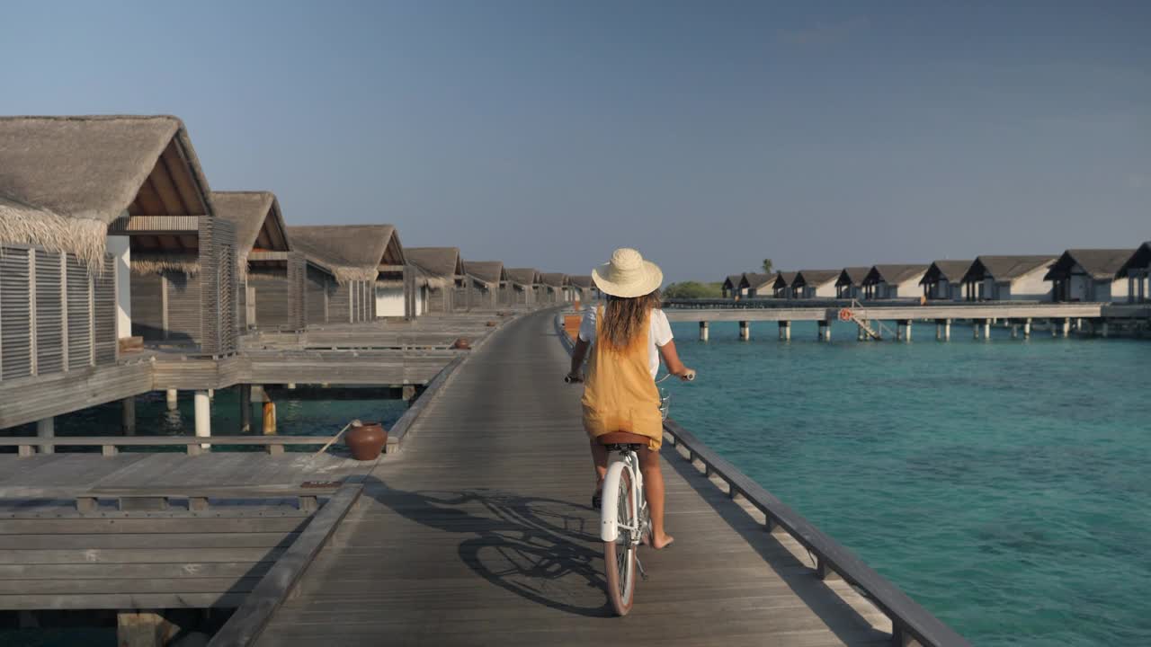 年轻女子骑着自行车在马尔代夫岛的旅游豪华度假村周围。视频素材