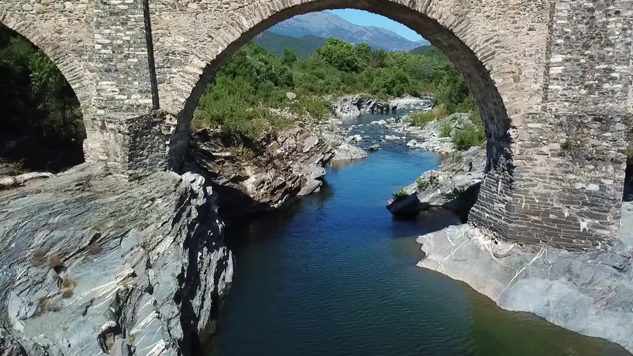 无人机飞过河边的一座桥。科西嘉山脉和常青的灌木林-玛其亚可见。视频素材