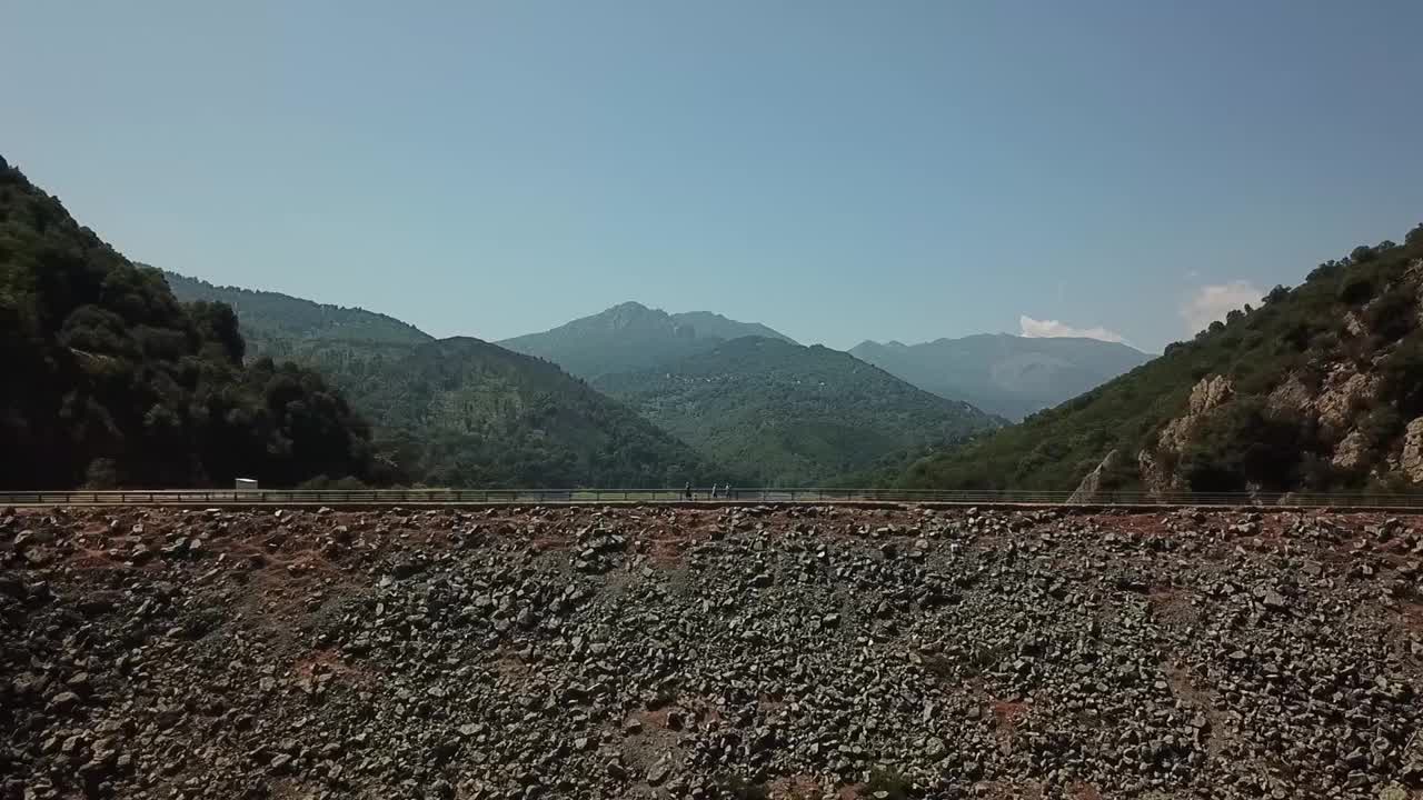 无人机向后飞过一座水坝。你可以看到科西嘉的山脉和常青的灌木林马吉亚。法国视频素材