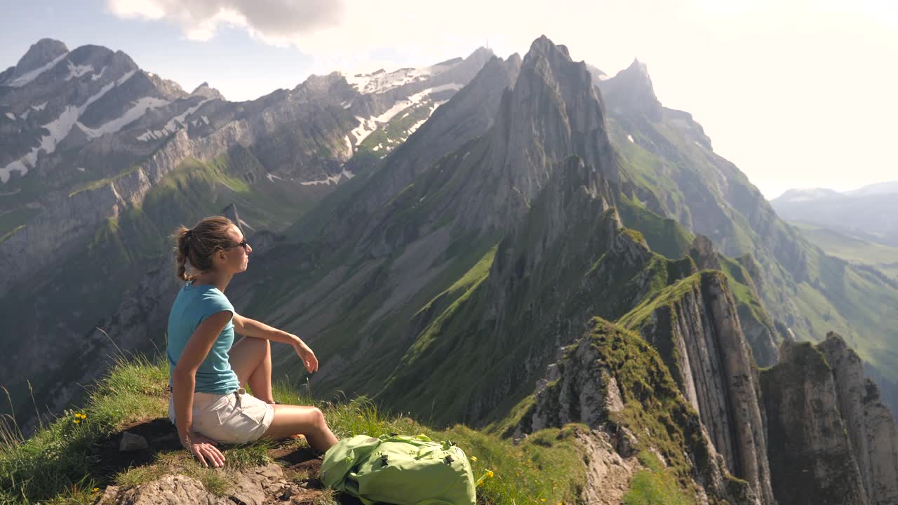 年轻女子在徒步旅行中凝视着令人惊叹的山脉景色。手臂张开视频素材