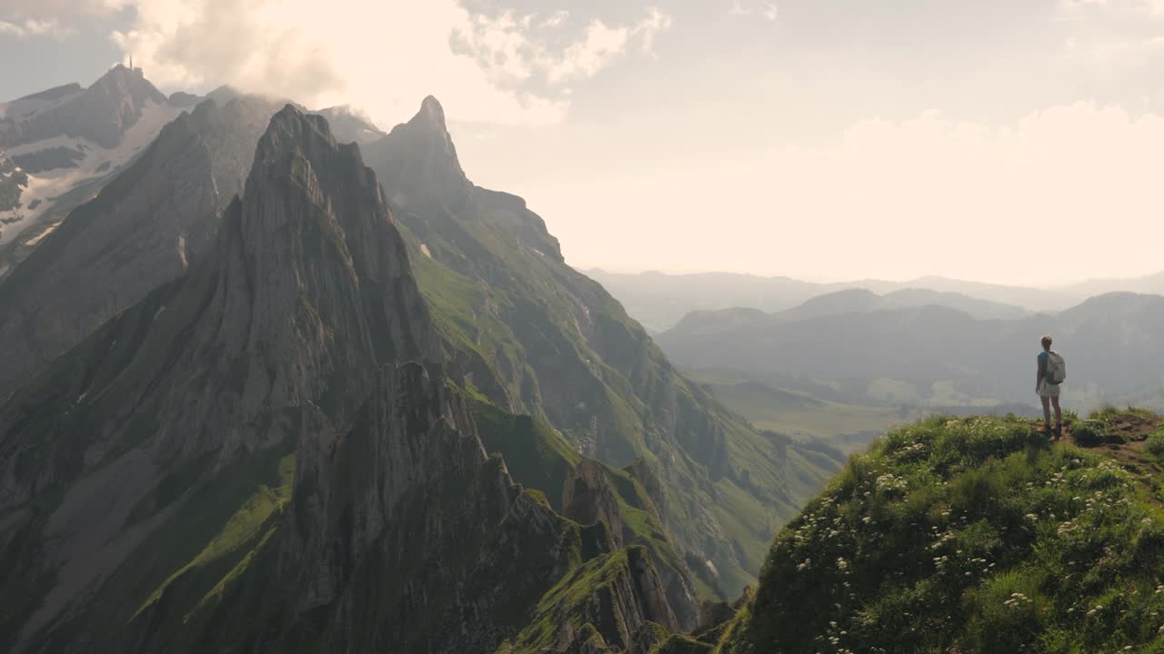 年轻的女徒步旅行者高举着手臂站在山顶上。视频素材