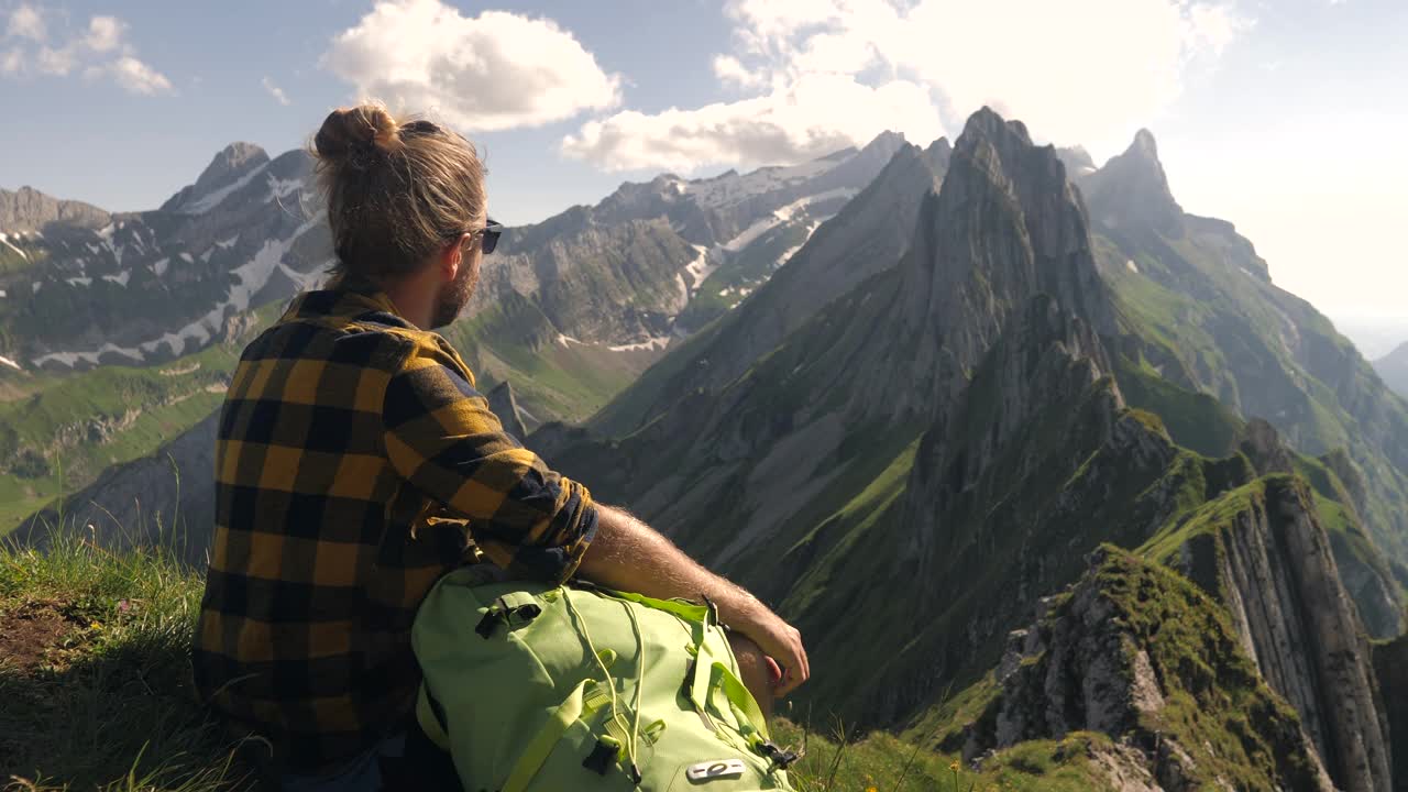 一个徒步旅行的年轻人凝视着令人惊叹的山脉景色。徒步旅行者坐在山顶上视频素材