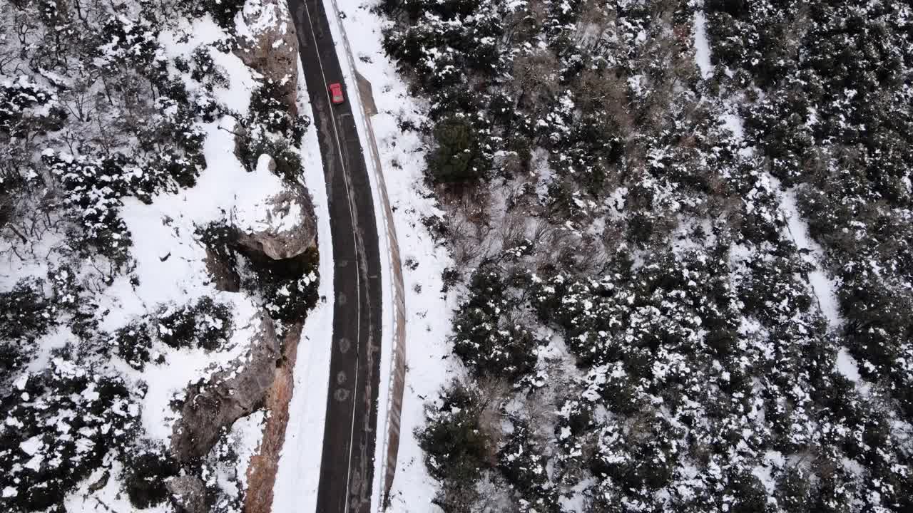 从无人机鸟瞰一辆红色汽车在冰雪路面上行驶在冬天探索当地景观，鸟瞰汽车在美丽的针叶林周围移动的区域。视频素材