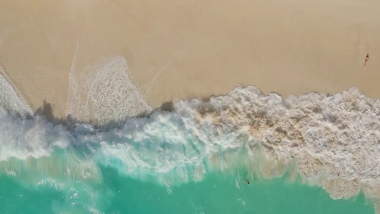 鸟瞰碧绿的海浪拍打着泡沫在光滑的沙滩上视频素材