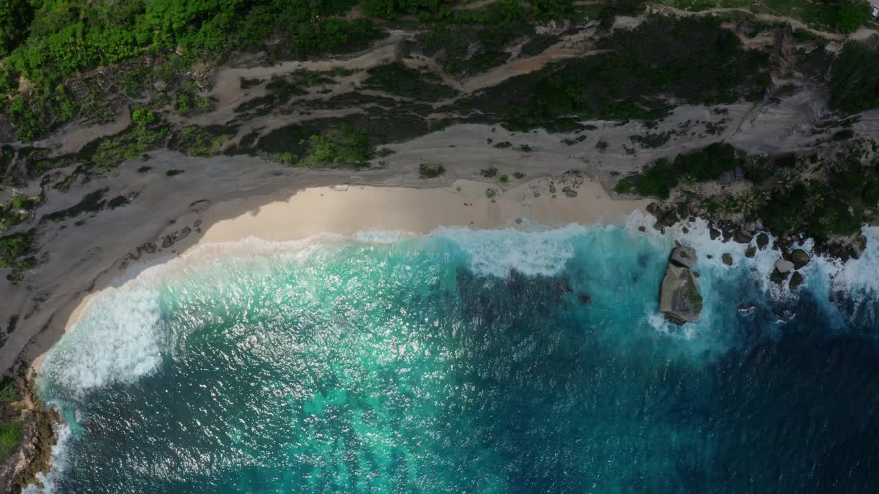 从上到下鸟瞰蔚蓝的海水，海浪冲击着野生的海滩视频素材