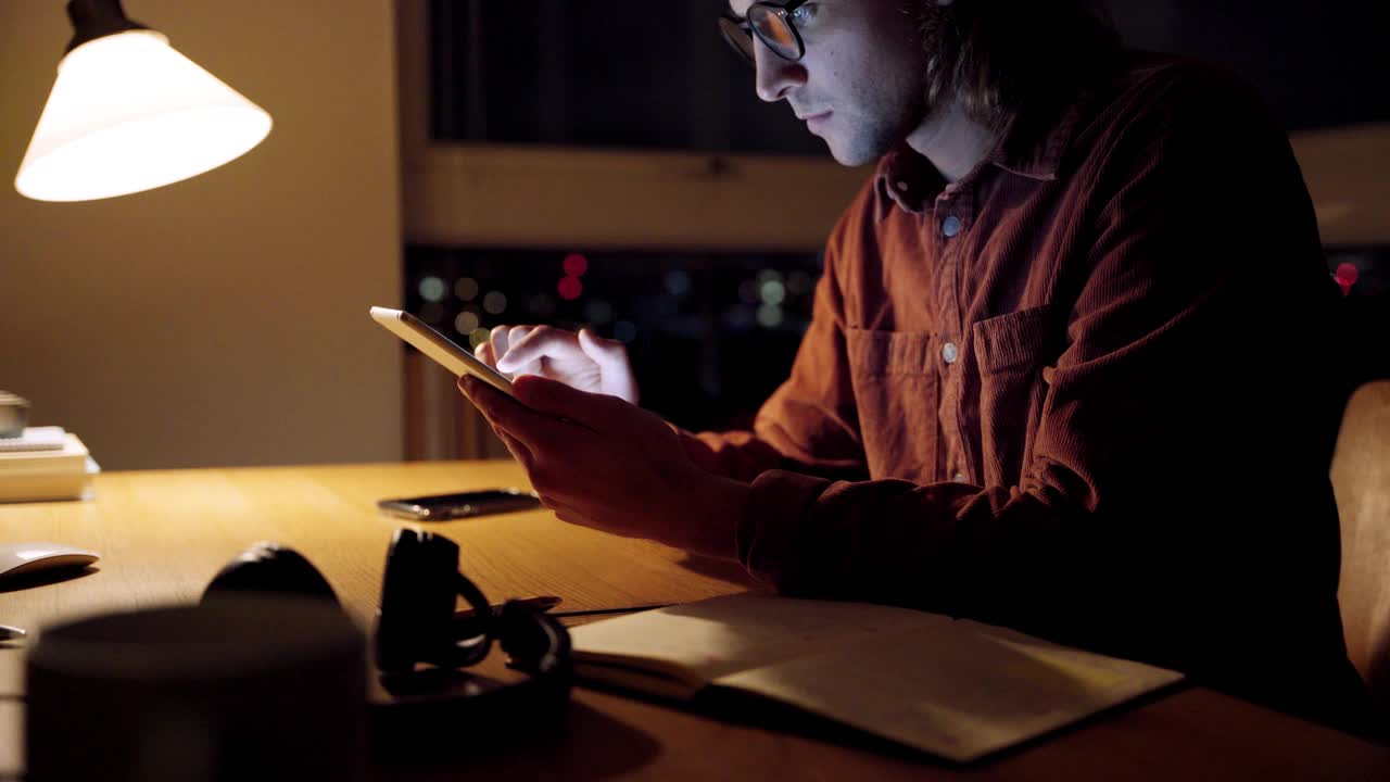 白种男性自由职业者晚上学习，坐在家里的办公桌上用ipad打字视频素材