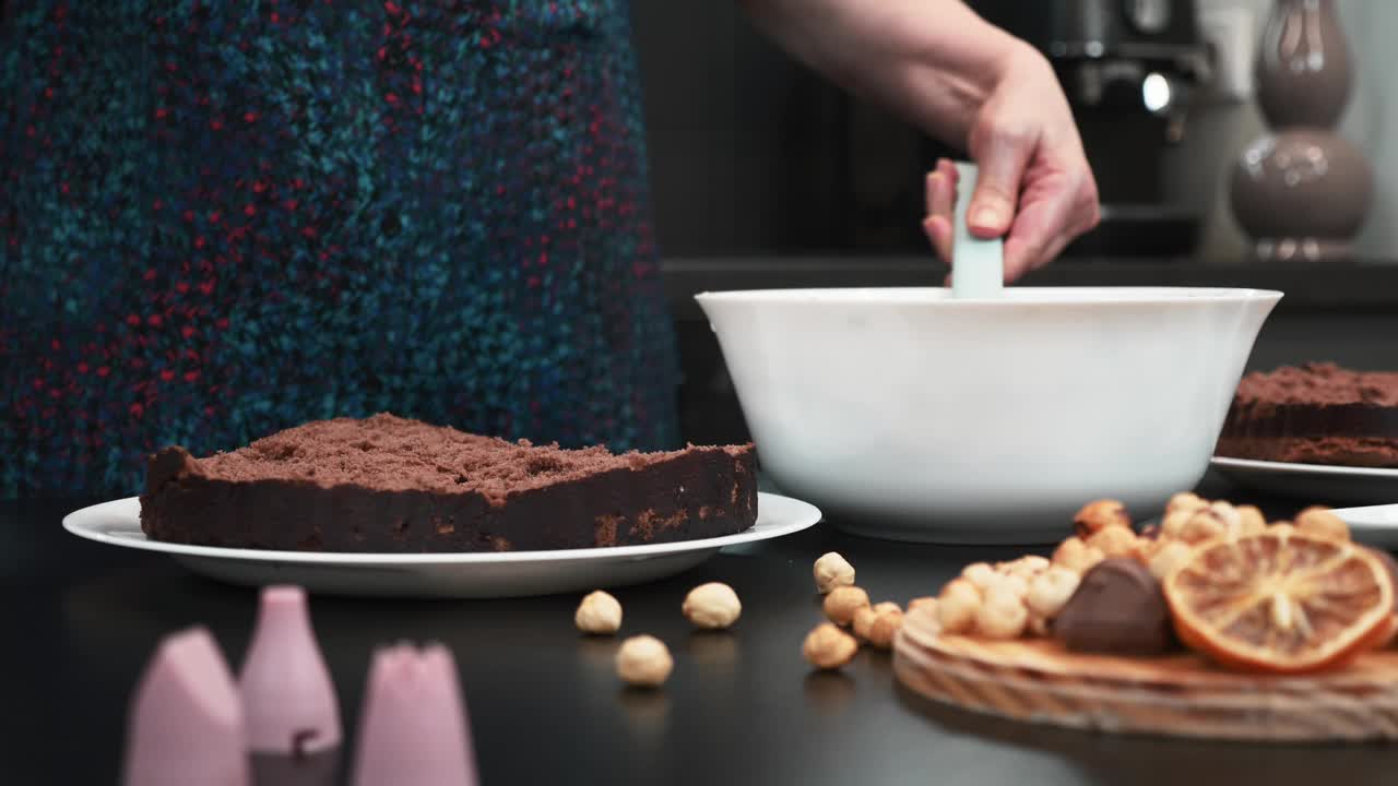 女人的手正在用白奶油和饼干做蛋糕。女面包师正在把奶油涂在巧克力蛋糕上。糕点师正在用奶油做巧克力蛋糕。烹饪和糕点技能视频素材