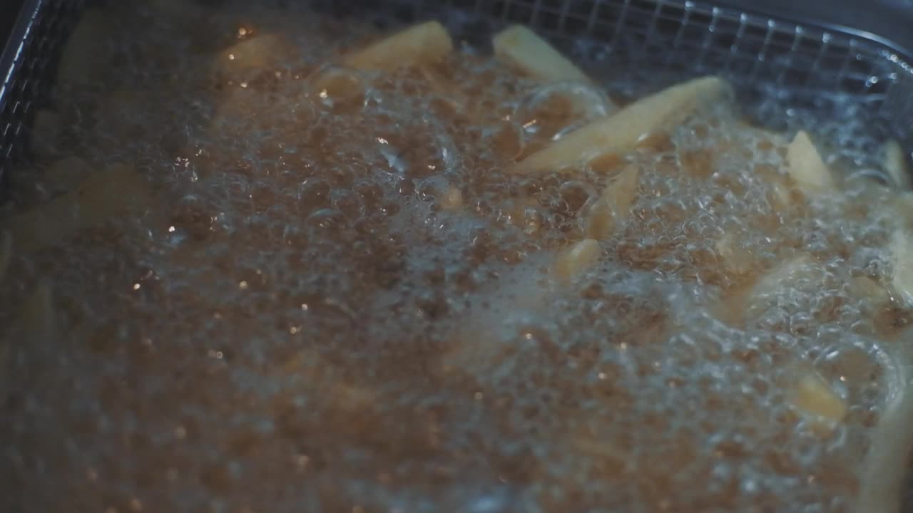 炸薯条在铁丝筐里，在热油里炸。特写慢动作镜头视频素材