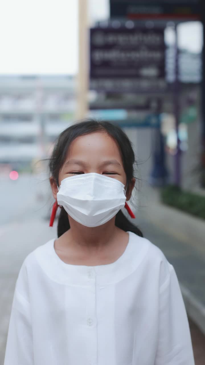 在冠状病毒大流行期间，亚洲女孩在口罩后面微笑，在城市的人行道上行走的4K垂直。视频素材