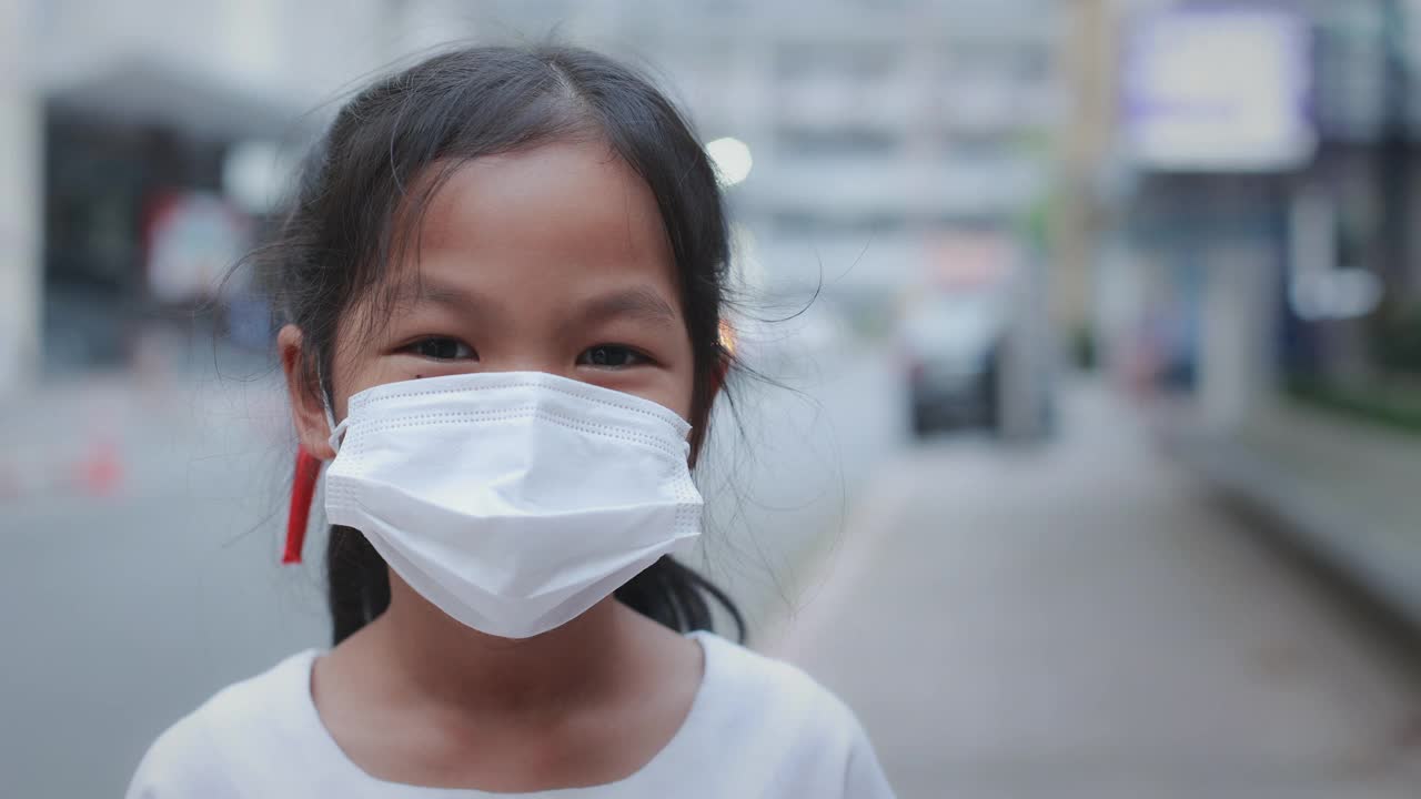 在新冠肺炎大流行期间，亚洲女童在口罩后微笑着站在城市人行道上的肖像。视频素材