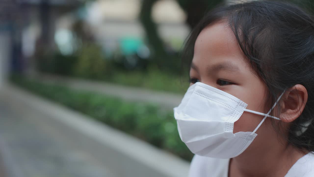 在新冠肺炎大流行期间，亚洲女孩戴着口罩站在人行道上微笑。视频素材