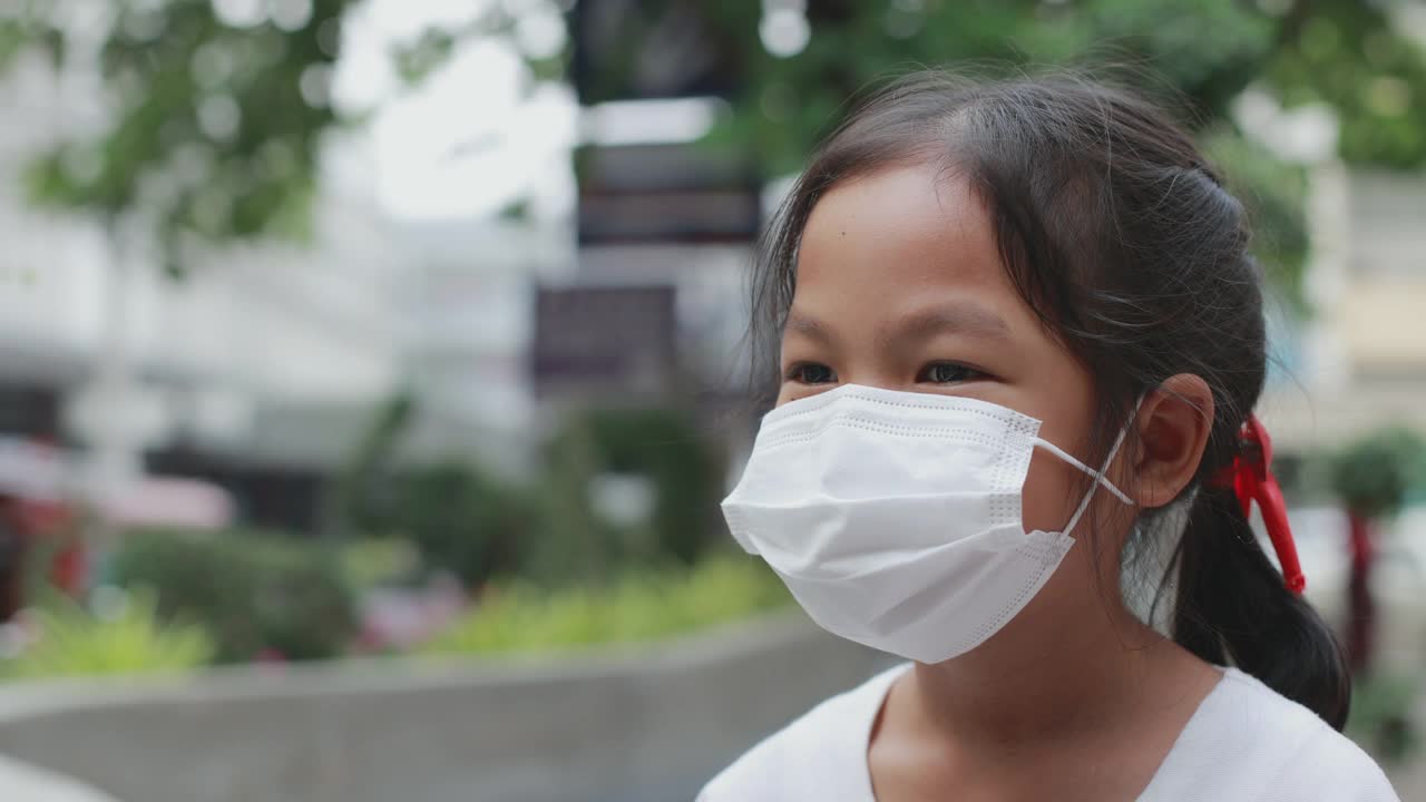 在新冠肺炎大流行期间，亚洲女孩戴着口罩站在人行道上微笑。视频素材