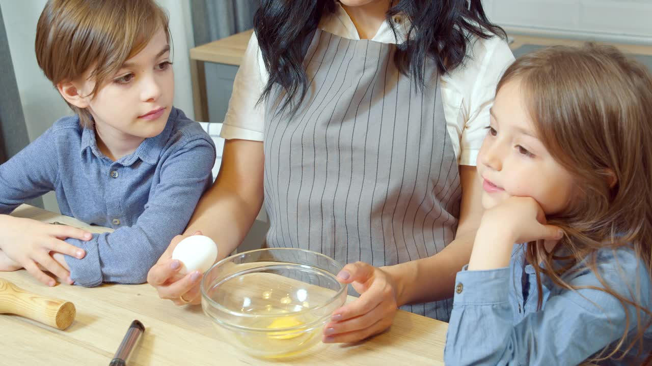 快乐的家庭为饼干准备面团。两个可爱的孩子男孩和女孩在厨房里帮助妈妈视频素材