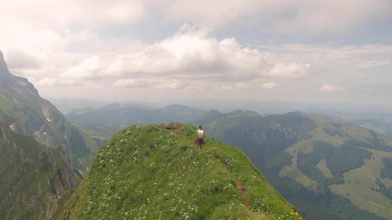 年轻的女徒步旅行者高举着手臂站在山顶上。视频素材