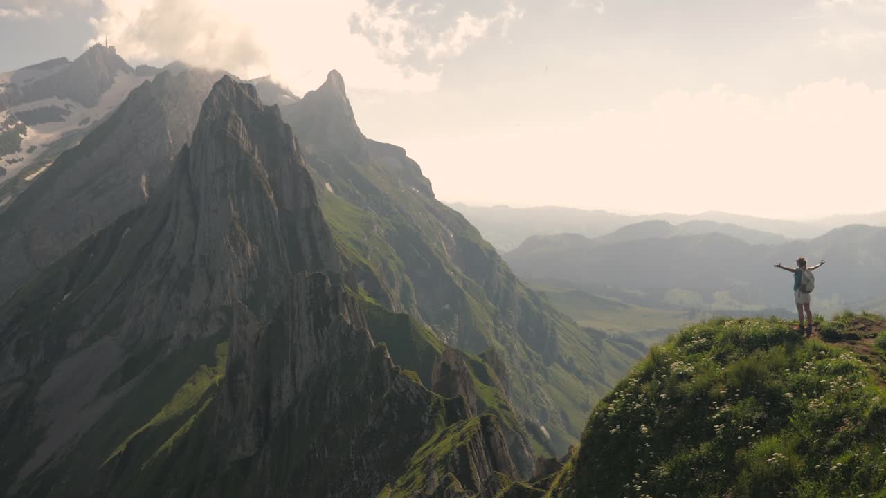 慢镜头:年轻的女徒步者站在山顶上，双臂高举。徒步旅行者考虑自然视频素材