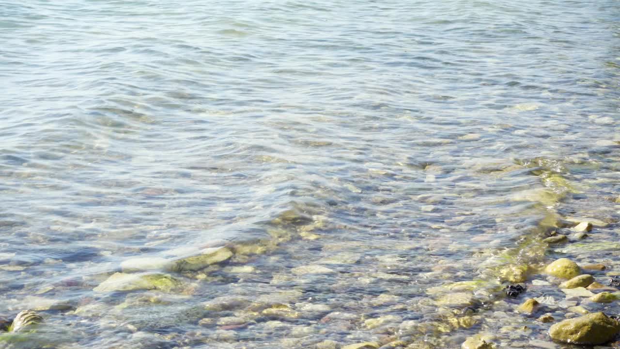 阳光明媚的地中海。浅水的波浪拍打着盐湖上陈旧的发霉的岩石视频素材