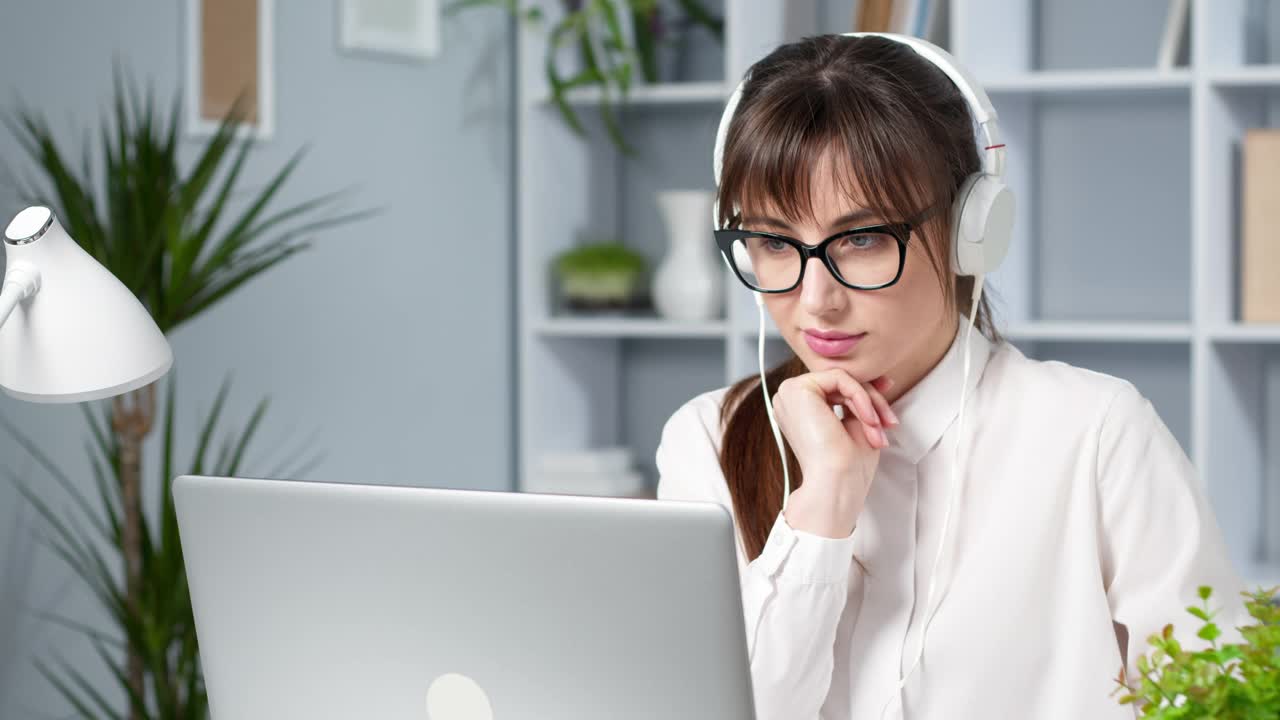 戴着耳机的女学生使用笔记本电脑远程学习。一位年轻女子正在观看在线教育研讨会。女商人在听视频会议。视频素材