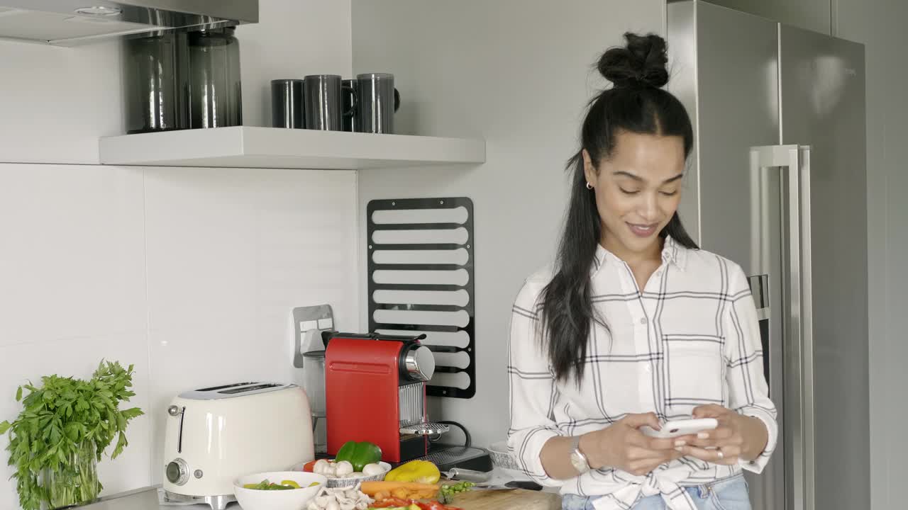 混血女人在厨房用她的智能手机发短信视频素材