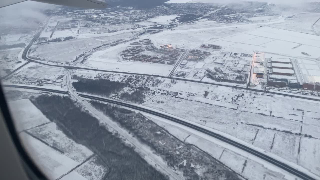 在冬季的圣彼得堡上空飞行，从飞机窗口可以看到白雪皑皑的郊区景观视频素材