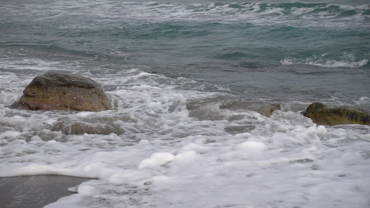 在克里米亚的诺维斯韦特村的沙滩上，黑海的泡沫波浪堆积在一块岩石上。没有人。早春多云视频素材