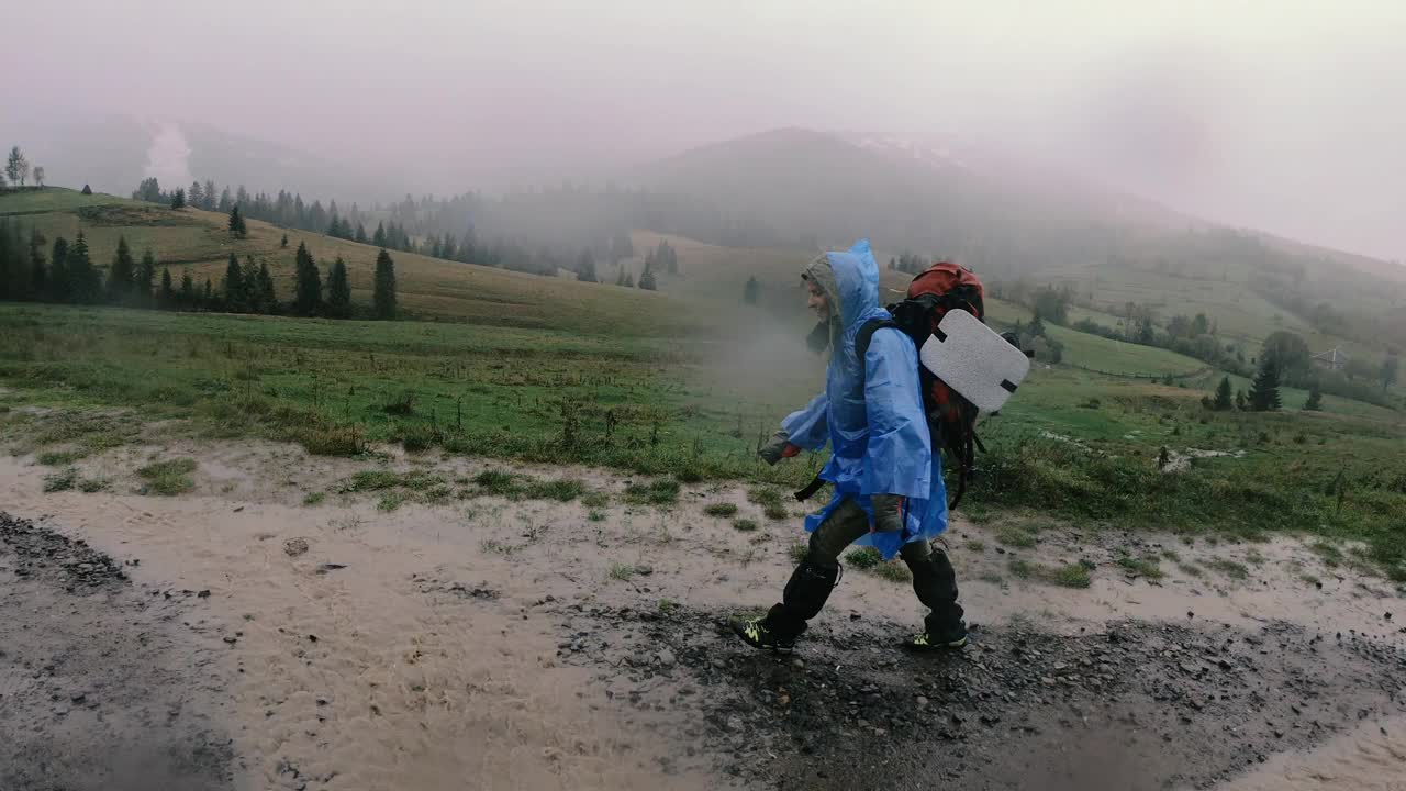 雨衣。一个女人穿着防水雨衣背着背包在雨中行走。视频素材