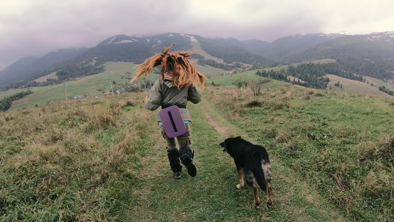 旅行。一个女孩牵着一只狗穿过草原，背景是群山。视频素材