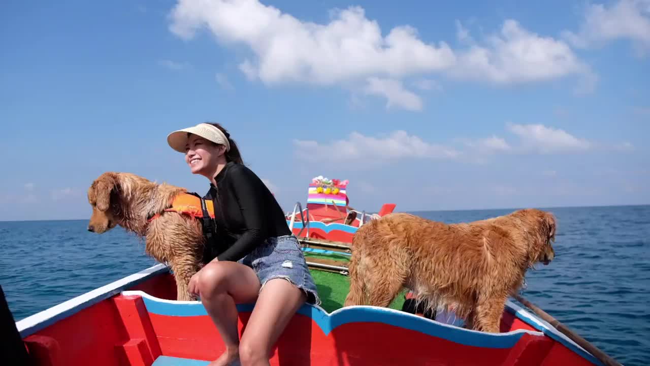 一个美丽的年轻亚洲女人与金毛猎犬与救生衣在船上玩的慢动作，而在海上航行视频素材