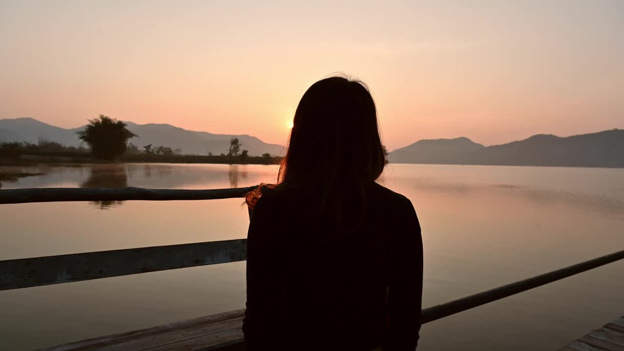 年轻的亚洲女子放松举起的木制码头上的手臂。在乡村水库的山上欣赏日出视频素材