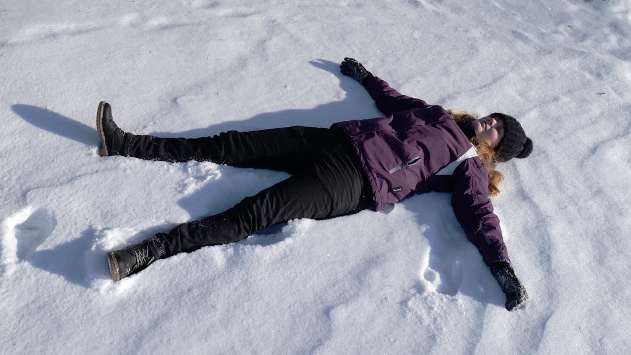 女孩躺在雪地里做了一个雪天使。女孩在雪中快乐视频素材