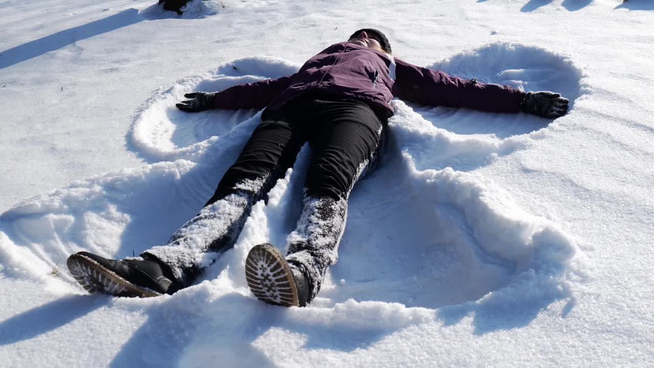 女孩躺在雪地里做了一个雪天使。女孩在雪中快乐视频素材