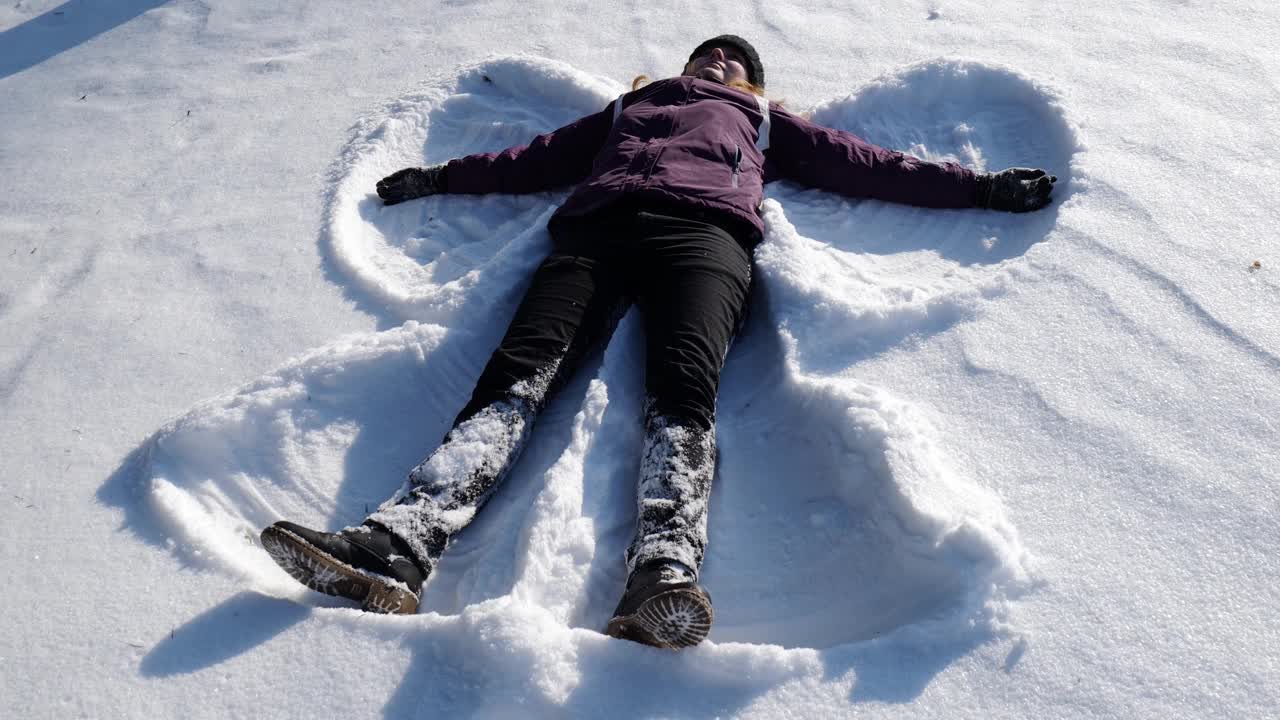 女孩躺在雪地里做了一个雪天使。女孩在雪中快乐视频素材