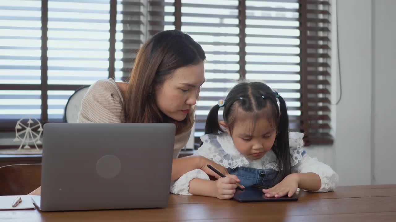 妈妈在家里用笔记本电脑工作，帮助女儿做作业视频素材