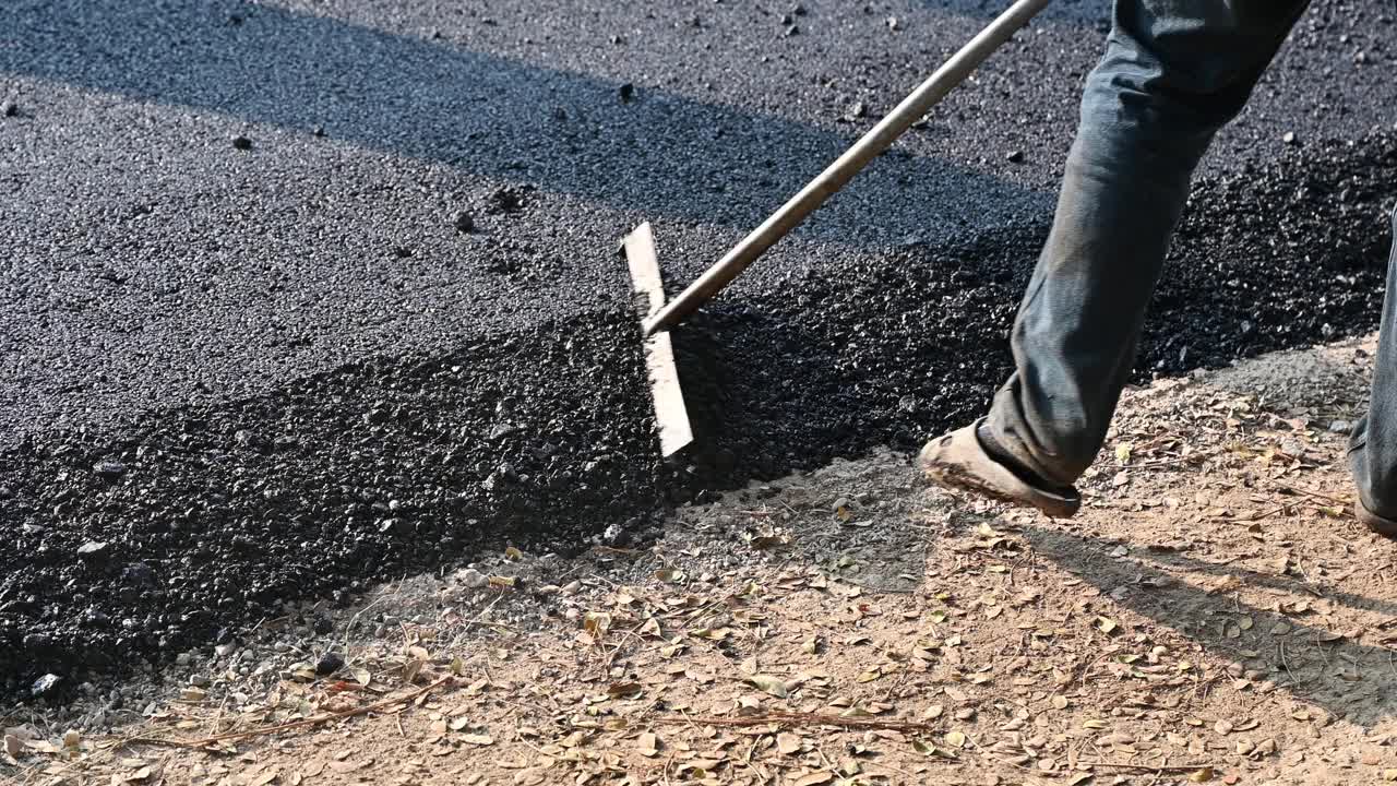 建筑工人用工具在高速公路上精确地铺平热拌沥青路面视频素材