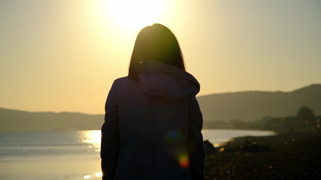 日落时分，一位年轻女子在海滩上双手合十，做了一个心形手势。视频素材