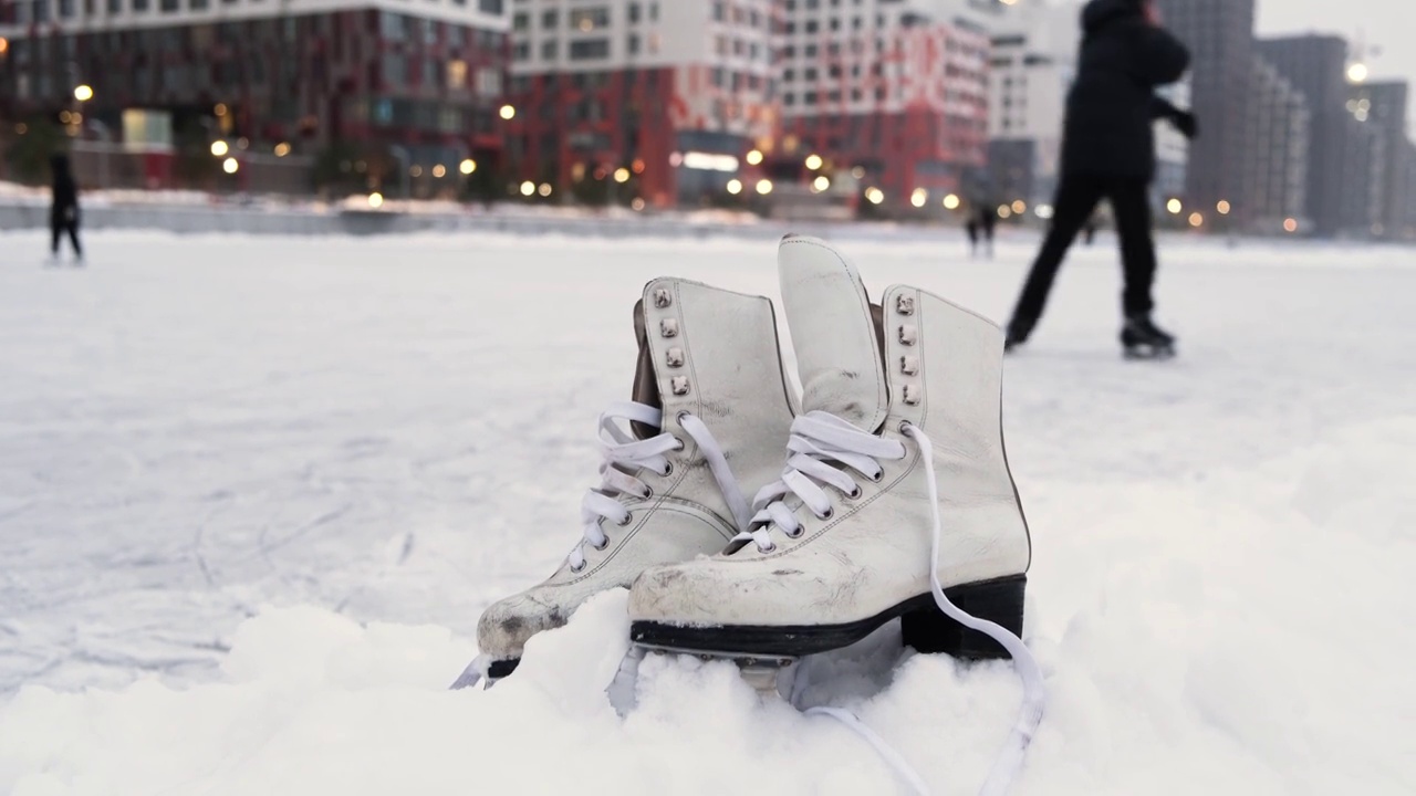 在现代城市的公共溜冰场附近，旧的白色溜冰鞋正在雪地上滑行。冬季户外活动概念。视频素材