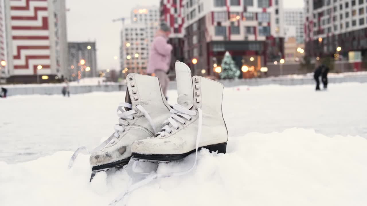 在现代城市的公共溜冰场附近，旧的白色溜冰鞋正在雪地上滑行。冬季户外活动概念。视频素材