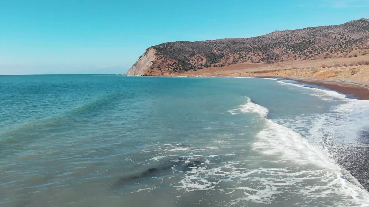 冬季阳光明媚的海面上有泡沫波浪的鸟瞰图。无人机滑翔在海洋海岸线上干燥的黄色岩石悬崖视频下载