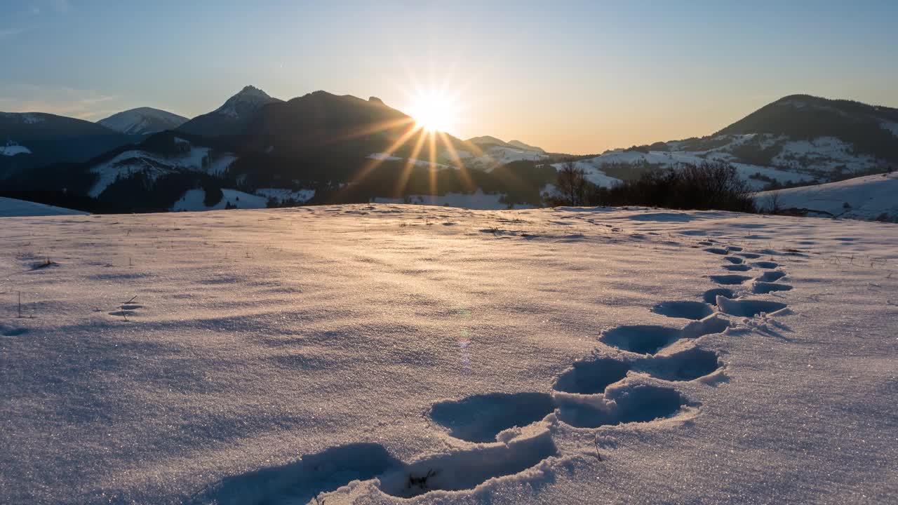 冬天的日落在冰冻的雪山景观在美丽的阳光灿烂的晚上自然与脚印在雪的时间流逝视频素材