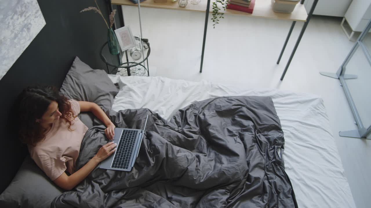 女人在床上用笔记本电脑打字的俯视图视频素材