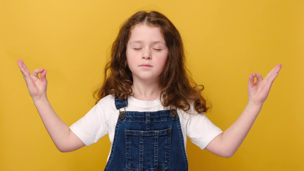 近距离的微笑沉思的学龄前小女孩的肖像，可爱的孩子闭着眼睛。幸福的概念，快乐的活动，好玩的孩子放松和冥想，在黄色的工作室背景孤立视频素材